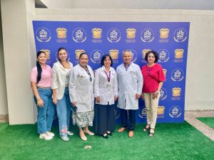 Grupo de seis profesionales médicos y administrativas del Hospital Universitario del Caribe posando de pie frente a un telón institucional azul con los logos del HUC 20 Años y la Gobernación de Bolívar.
